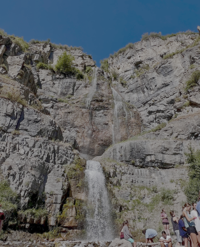Tall Stewart Falls waterfall cascading down a rocky cliff under a clear blue sky.